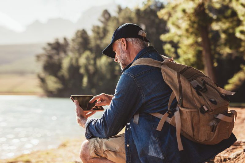 Mature man on hike in nature using digital tablet