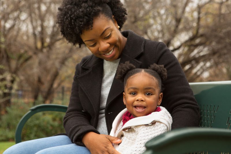 Mother and young daughter sitting on park bench