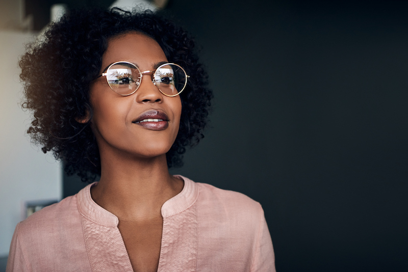 Smiling businesswoman wearing glasses looking deep in thought while standing alone in a modern office